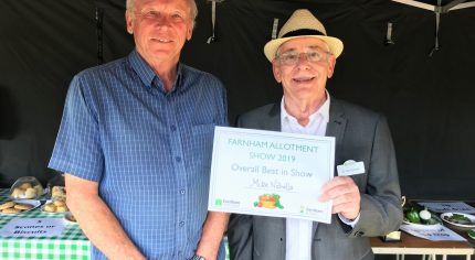 Two men in a marquee. Man on right presents a certificate.