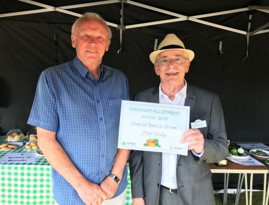Two men in a marquee. Man on right presents a certificate.