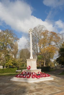 Stone war memorial in park setting. Poppy wreaths at base.