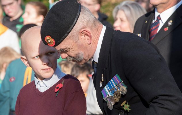 Man in beret and wearing medals talks to young boy