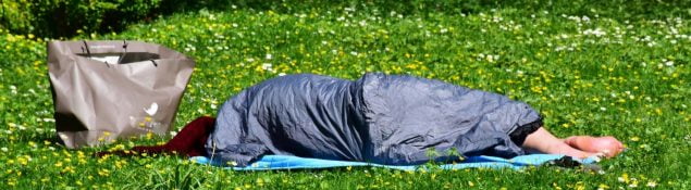 Rough sleeper under sleeping bag on grass