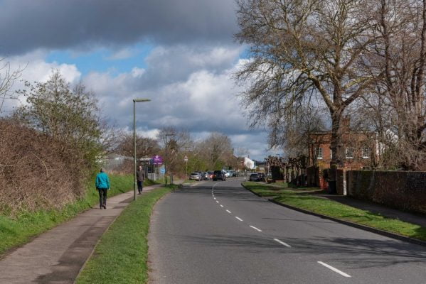 View along a tree lined road. People walking on the grass lined footpath.