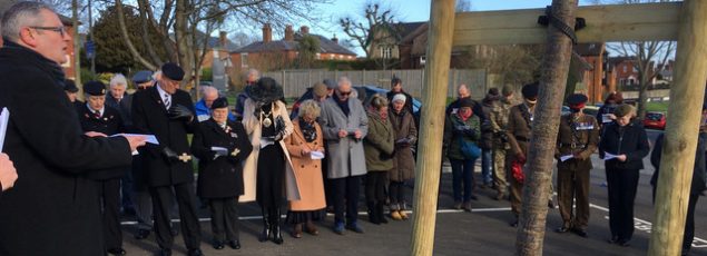 Gathering of people at a tree planting ceremony. Tree trunks in foreground.
