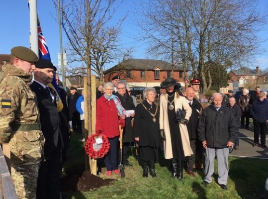 Group of people standing in semi circle. Trees and union flag in background