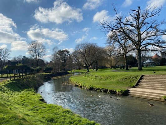 Meandering river, grass banks, blue sky and trees in background. Winter