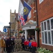 Group of adults and children in front of building. Commonwealth flag and Union flag flying on side of building