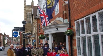 Group of adults and children in front of building. Commonwealth flag and Union flag flying on side of building