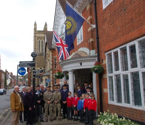 Group of adults and children in front of building. Commonwealth flag and Union flag flying on side of building