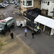 Aerial photo of four people in front of vehicles and a marquee.