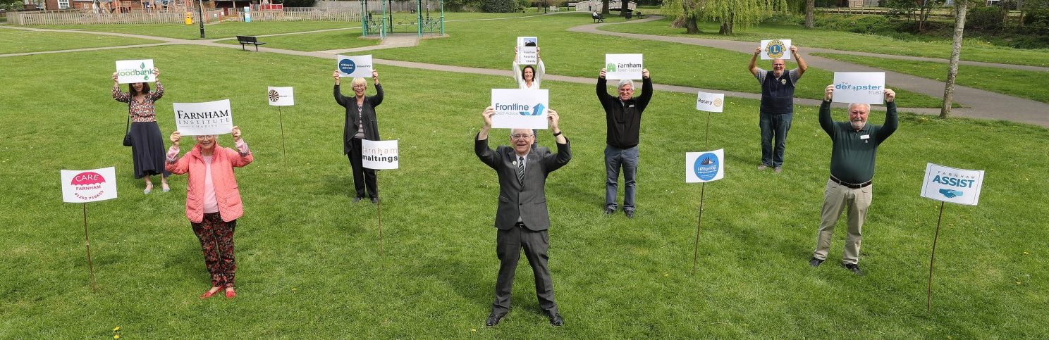 Group of people standing 2m apart on grass holding signs.