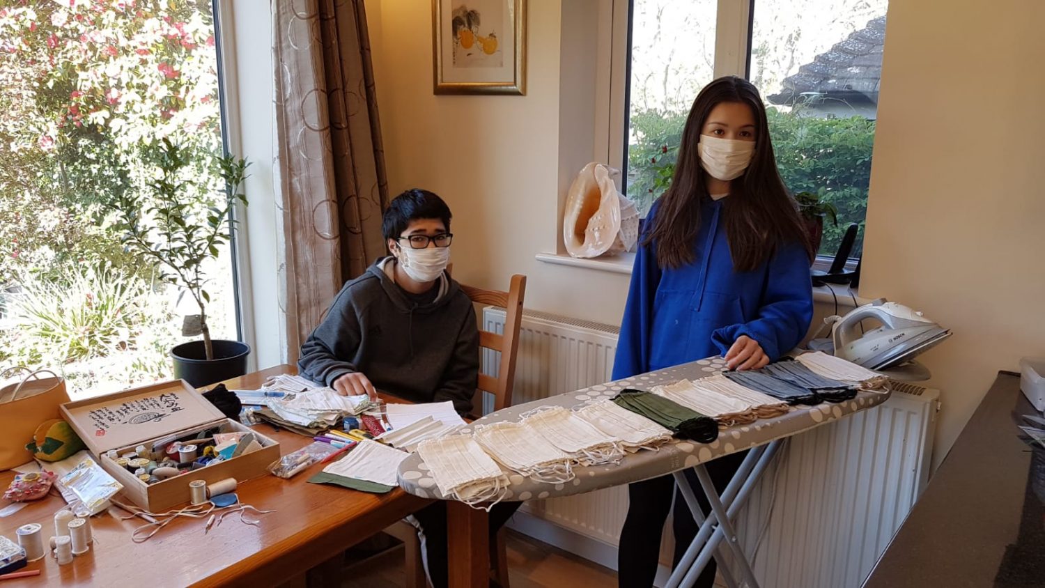 Boy and girl with face masks they have made on an ironing board