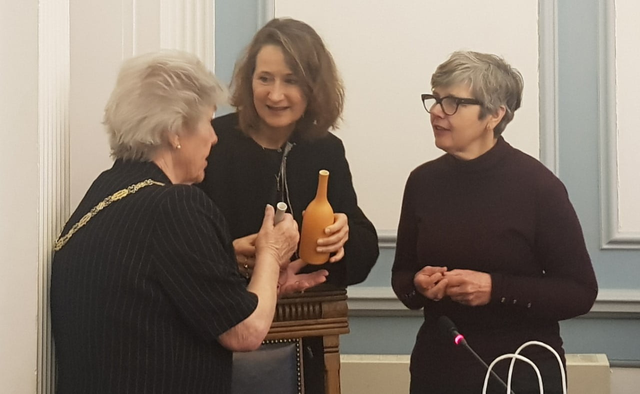 Three females talking. Two are holding ceramic bottles