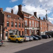 Row of parked cars in front of red brick shops and businesses. Town centre