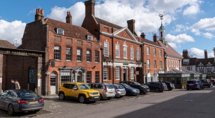 Row of parked cars in front of red brick shops and businesses. Town centre