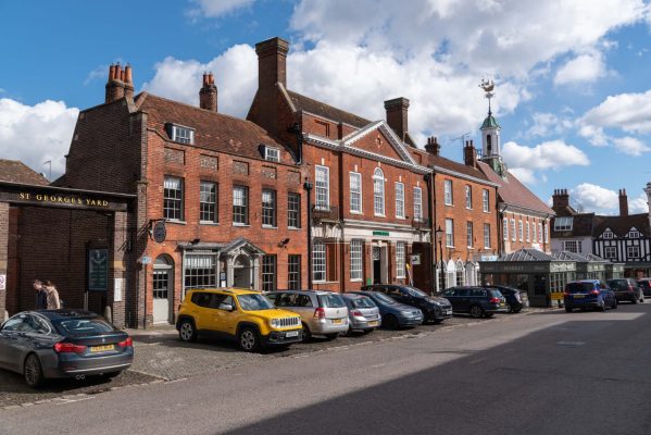 Row of parked cars in front of red bricked shops and businesses. Town centre