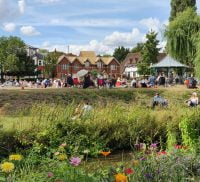 River and wildflowers in the foreground. Bandstand and people in the distance