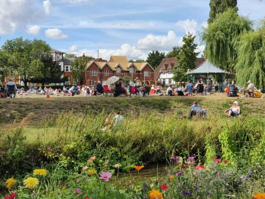 River and wildflowers in the foreground. Bandstand and people in the distance