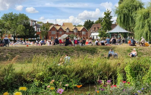 River and wildflowers in the foreground. Bandstand and people in the distance