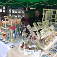 Two females standing behind a stall selling craft items.