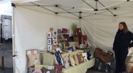 Market stall displaying cushions and craft items.