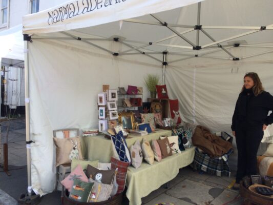 Market stall displaying cushions and craft items.