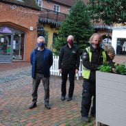 Group of five people standing in a shopping yard. Two men on right tend to flowers in a large planter.