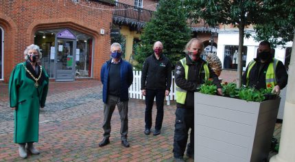 Group of five people standing in a shopping yard. Two men on right tend to flowers in a large planter.