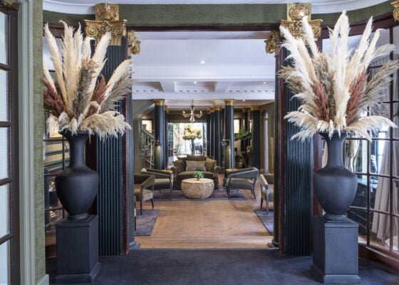 View through a doorway at a seating area. Door flanked by large vases of grass.