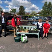 Two adults and two children standing next to a bench filled with items to make a hanging basket.