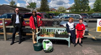 Two adults and two children standing next to a bench filled with items to make a hanging basket.