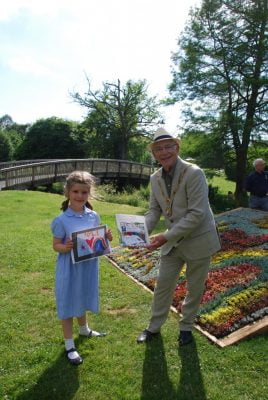 Young girl holds a drawing and receiving a prize from the Mayor.