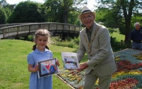 Young girl holds a drawing and receiving a prize from the Mayor.