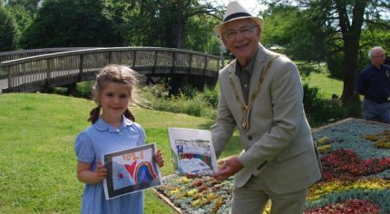 Young girl holds a drawing and receiving a prize from the Mayor.