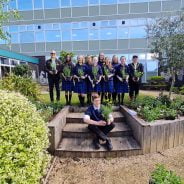 Group of students holding plant and standing on a raised grass area.