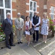 Five people standing in a line in front of a red brick building.