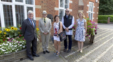 Five people standing in a line in front of a red brick building.