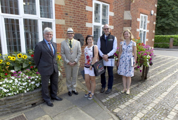 Five people standing in a line in front of a red brick building.