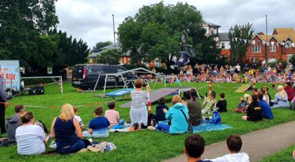 Crowd of people sitting on grass watching a stunt bike rider