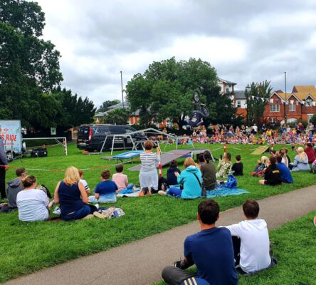 Crowd of people sitting on grass watching a stunt bike rider