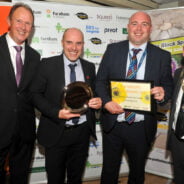 Four males standing in row. One holding a trophy and one a framed certificate.