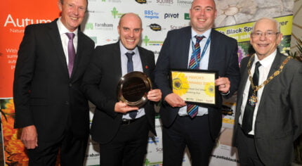 Four males standing in row. One holding a trophy and one a framed certificate.