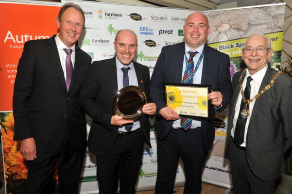 Four males standing in row. One holding a trophy and one a framed certificate.