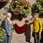 Male and female remove a red cloth to reveal a plaque on wall