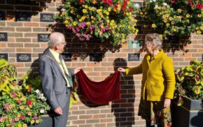 Male and female remove a red cloth to reveal a plaque on wall