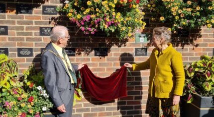 Male and female remove a red cloth to reveal a plaque on wall