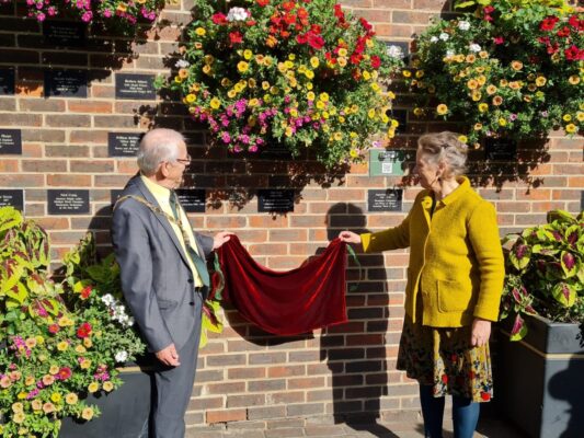 Male and female remove a red cloth to reveal a plaque on wall