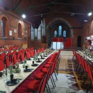 3 long tables set for dinner with red chairs inside church.