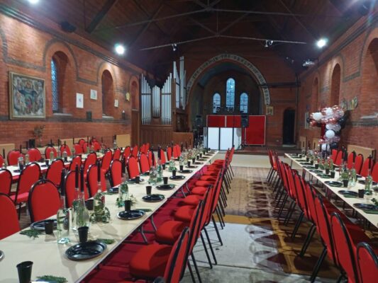 3 long tables set for dinner with red chairs inside church.