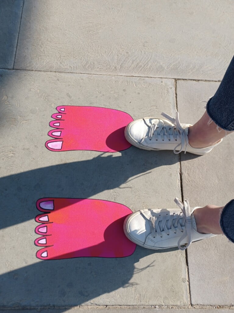Pair of feet standing on pink monster footprints.