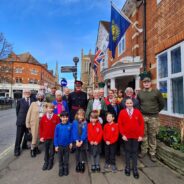 Schoolchildren and adults stand under a flag